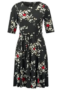 Robe noire longueur genou avec imprimé floral blanc et beige, accents de fleurs rouges, manches courtes, col rond et ceinture à nouer en tissu à la taille.