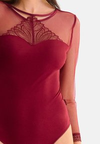 Body bordeaux avec des manches longues en maille transparente, des détails en dentelle au col et des bretelles fines. Texture lisse avec un design ajusté.
