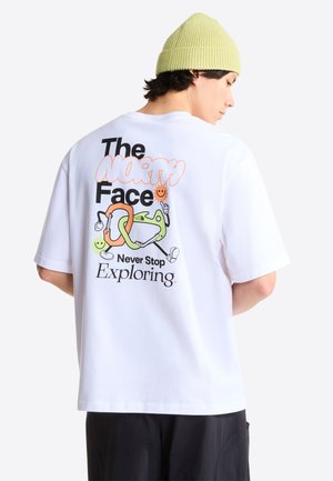 Mann trägt weißes T-Shirt mit farbenfrohem Karabiner-Grafik, Text "The North Face Never Stop Exploring" und eine hellgrüne Mütze.
