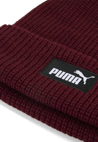 Bordeaux gebreide muts met een geribbelde textuur en een zwart rechthoekig label met het witte "PUMA" logo en de springende puma afbeelding.
