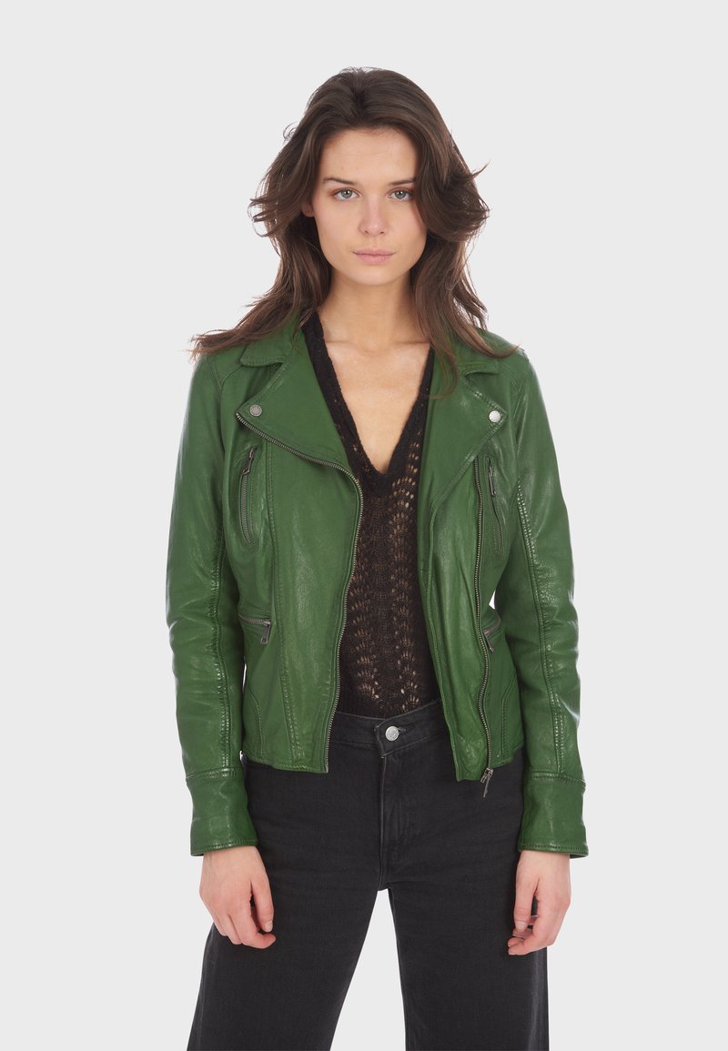 Groene leren motorjack met ritszakken, reverskraag en gladde textuur, gedragen over een zwart gebreid topje en zwarte jeans.