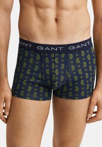 Marineblaue Boxershorts mit Paisley-Muster in Grün und Gelb, ausgestattet mit einem weichen Bund, auf dem der Markenname in Weiß gedruckt ist.