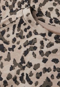 Látka s leopardím vzorem v béžové barvě se tmavě hnědými a černými skvrnami. Má jemnou texturu a kulatý výstřih. Detailní pohled na materiál.