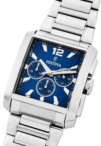 Srebrna ura iz nerjavečega jekla z kvadratnim modrim številčnico. Ima tri majhne številčnice, bele oznake za ure in izrazito 12 na vrhu.