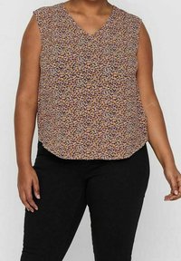 Kwiatowy top bez rękawów z dekoltem w kształcie litery V, z wielokolorowym wzorem na beżowym tle, zestawiony z czarnymi spodniami. Miękki materiał i luźny krój.