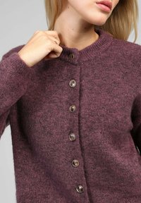 Cardigan en tricot bordeaux avec un col rond, six boutons et une texture douce. Présente des manches longues et une coupe décontractée.