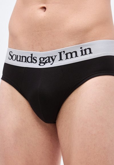 Μαύρο σλιπ με αντίθετη γκρι ζώνη μέσης που φέρει το κείμενο «Sounds gay I'm in» εμφανώς γραμμένο με μαύρη γραμματοσειρά.