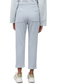 Světle modré tepláky s elastickým pasem, dvěma zadními kapsami, rovný střih a délka ke kotníkům, doplněné o bílé a zelené tenisky.