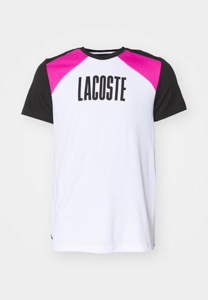 Valge lühikeste varrukatega T-särk roosa ja musta raglanvarrukaga, mille esiküljel on suur "LACOSTE" tekst ja väike logo hemmi juures.