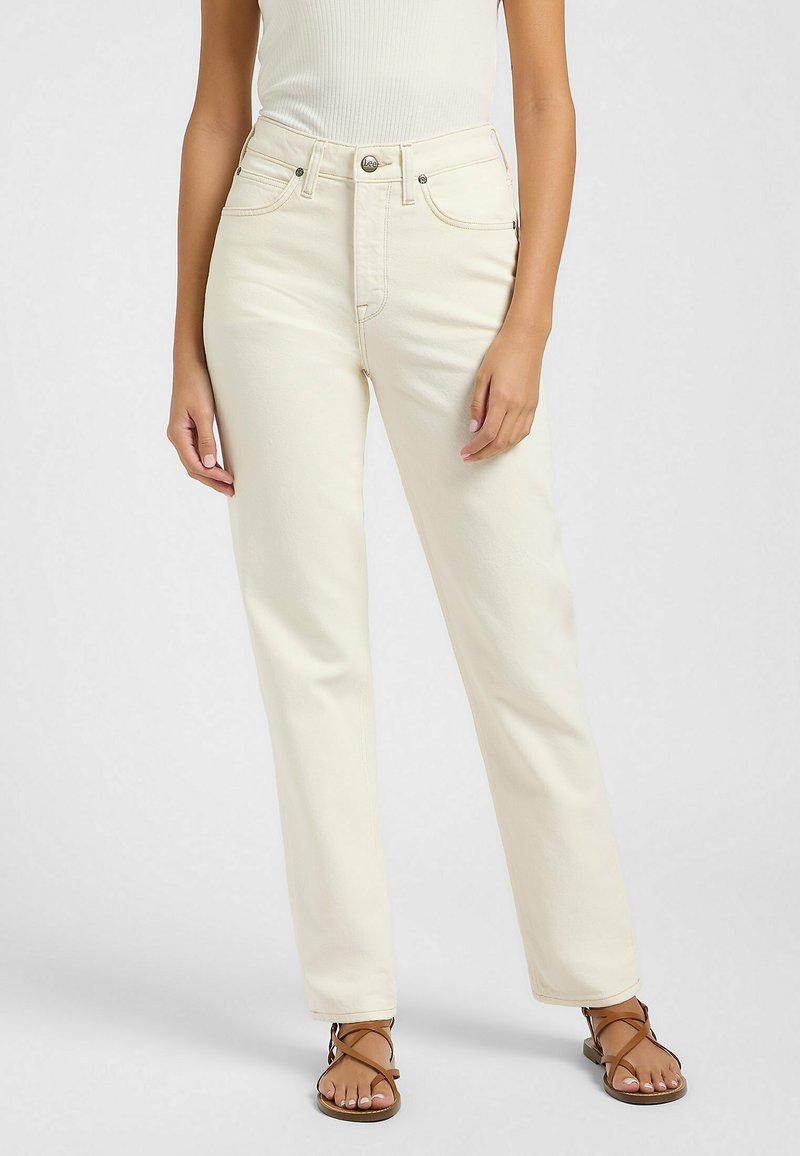 Jeans crema de cintura alta con un corte recto, cinco bolsillos y costuras de contraste. Combinados con sandalias marrones de tiras y una blusa ajustada.