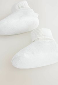 Bottines en tissu blanc avec une finition douce, des poignets de cheville côtelés et un design à bout arrondi. Texture subtile et une petite étiquette logo visible.