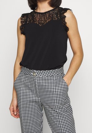 Zwart topje met kantdetails op de schouders, gecombineerd met zwart-witte broek met een ruitpatroon, hoge taille en zakken.