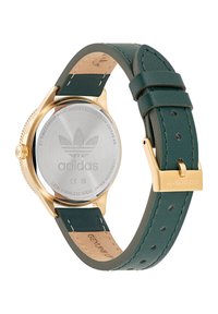 Auksinės spalvos nerūdijančio plieno laikrodis su žalia oda dirželiu. Yra tekstūruota paviršiaus, sagties užsegimas ir išgraviruotas Adidas logotipas ant nugaros.