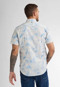 Korte mouw shirt in lichtbeige stof met blauwe bloemenpatronen. Voorzien van een standaardkraag en een gebogen zoom, met complexe details.