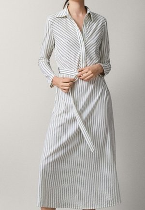Sukienka koszulowa w lekkim materiale z kołnierzykiem, długimi rękawami i wiązaniem w pasie. Posiada pionowe granatowe paski na białym tle.