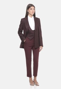 Completo in tre pezzi bordeaux con design a righe sottili, giacca monopetto, gilet aderente e pantaloni tapered. Camicia bianca con colletto sotto.