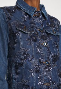 Dżinsowa kurtka z haftem z kwiatów cekinowych w granatowym kolorze. Posiada klasyczny kołnierz, przednie kieszenie i dekoracyjne guzików w złotym kolorze.