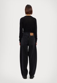 Mustat pitkät hihatoppi ja korkeavyötäröiset, leveälahkeiset mustat farkut, joissa on teksturoitu kangas. Nahkainen logo-patch takana vyötärön kohdalla.