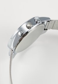 Silver metal wristwatch featuring a polished case, round shape, two push buttons, and textured mesh strap. Plain watch face and minimal detailing.