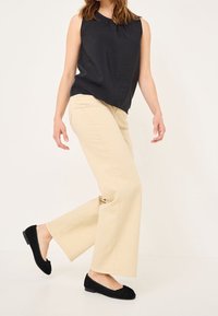 Svart ärmlös topp, beige vida byxor och svarta mockaskor med rosett. Enkel design och slät textur.