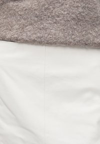 Siv pleteni zgornji del z puhastim videzom, kombiniran s gladko belo usnjeno krilom. Zgornji del ima rahlo spuščen rob čez pas.