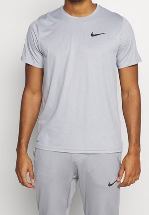 Mężczyzna ubrany w jasnoszary zestaw sportowy Nike, koszulka z krótkim rękawem i spodnie, czarne logo Nike na klatce piersiowej i udzie.