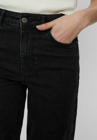 Černé džíny z denimu s klasickým střihem, které mají přední kapsy, kovové zapínání na knoflík a jemné švy kolem švů.