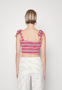 Top corto de tejido fruncido rojo y blanco con tirantes tipo lazo en los hombros. Presenta un patrón texturizado y un ajuste ceñido al cuerpo, combinado con pantalones blancos de cintura alta.