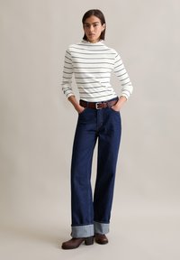 Haut rayé blanc à manches longues avec un col à volants, associé à un jean large bleu foncé avec un ourlet en denim retroussé et une ceinture en cuir marron.