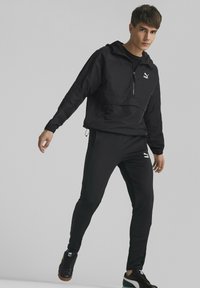 Svart sportsjakke med hette og frontlomme, paret med matchende tettsittende bukser. Begge har subtile logo detaljer og en jevn tekstur.