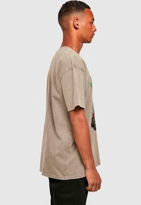 Short-sleeve, loose-fitting beige t-shirt made of soft fabric, featuring a colorful graphic design on the front and visible stitching details.
