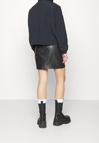 Svart läderminikjol, tillsammans med en svart bomberjacka. Modellen har på sig kraftiga svarta stövlar och vita strumpor med svarta detaljer, vilket ger en avslappnad stil.