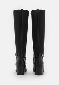Botas altas de cuero negro y tela con tacones cuadrados y correas decorativas en la parte trasera, mostradas desde la parte posterior sobre un fondo blanco.