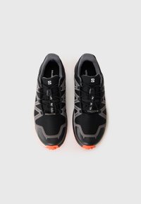 Black athletic shoes with gray accents. Features a textured upper, mesh panels, and a distinctive lacing system. Bright orange outsole detail.
