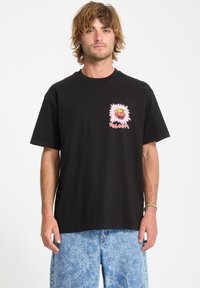 Camiseta de algodón negra de manga corta con un gráfico colorido en el lado izquierdo del pecho. Estilizada con pantalones cortos de tejano azul claro con efecto de lavado ácido.