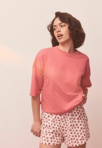 Lyserød bomulds t-shirt med korte ærmer kombineret med hvide shorts med et rødt hjerte mønster. Casual pasform med et afslappet design.