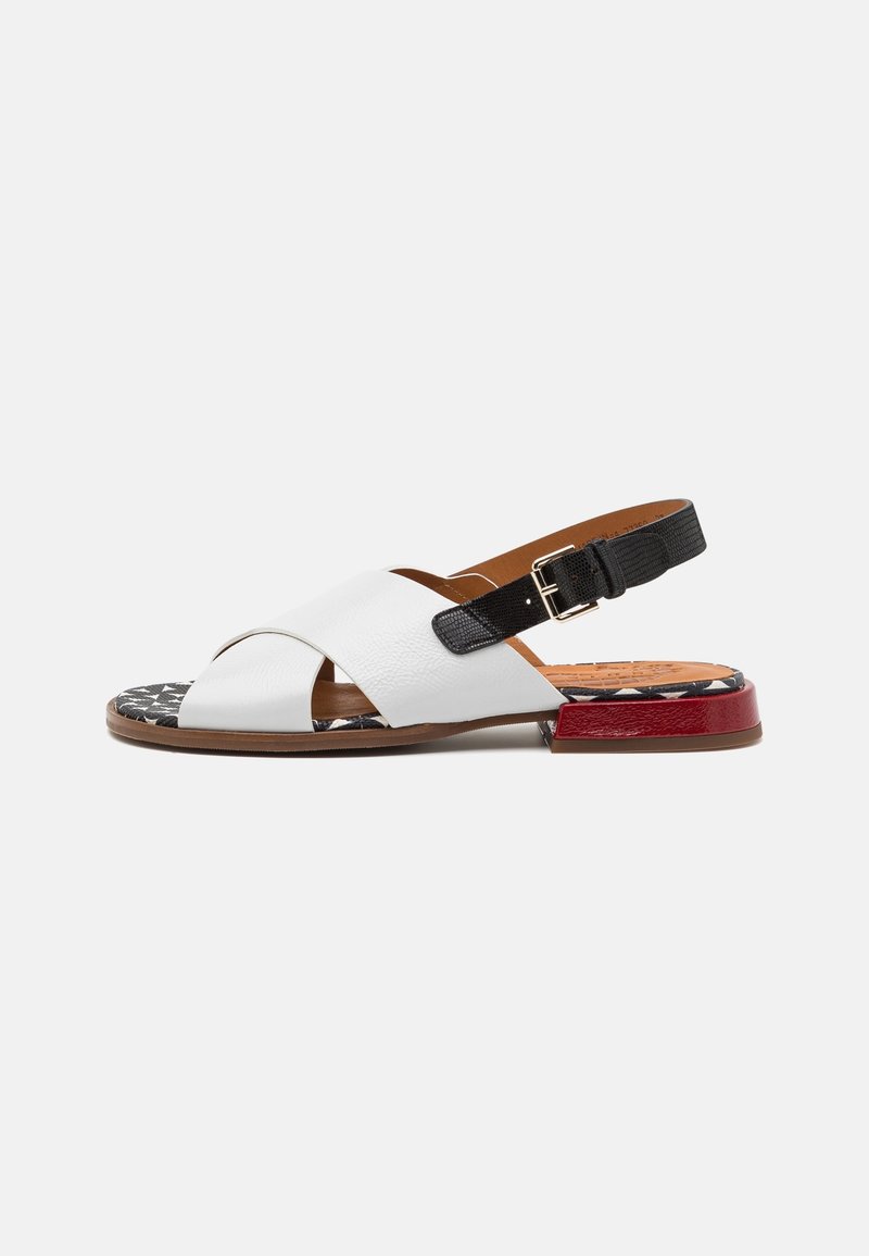 Sandale à petit talon avec des brides croisées en cuir blanc, une bride noire réglable avec boucle, une semelle à motif et un petit détail rouge au talon.