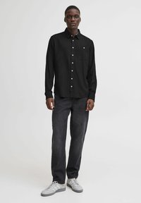 Svart langermet skjorte med knapper i kragen og lomme foran, parret med mørke jeans og grå joggesko med hvite snører.