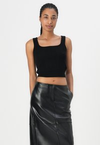 Svart strikket crop-top med firkantet utringning. Kombinert med et langt, glinsende svart skinnskjørt med en søm nedover fronten.