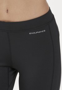 Svarta atletiska leggings i stretchtyg, med en platt midja och subtila sömmar, märkta med ordet "ENDURANCE" i vitt.