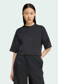 Felpa nera corta con maniche corte. Presenta tre strisce verticali in una texture nera lucida lungo un lato. Tessuto morbido con branding minimo.