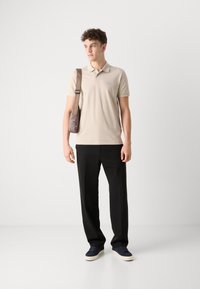 Beige polo skjorte, svarte bukser, marineblå sneakers. Slim fit, kortermet, minimal merkevare. Brun crossover-veske over skulderen.
