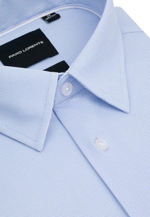 Jasnoniebieska teksturowana koszula męska z kołnierzem w szpic, białymi guzikami i czarną metką "PAKO LORENTE" wewnątrz kołnierza.