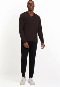 Donkerbruin gebreide trui met V-hals, gecombineerd met zwarte nauwsluitende broek en witte sneakers. Glad materiaal en een ontspannen pasvorm.