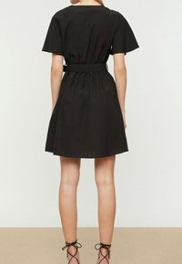 Robe noire à manches courtes en tissu léger, cintrée à la taille avec une ceinture, présentant une jupe évasée et des lignes simples et épurées.