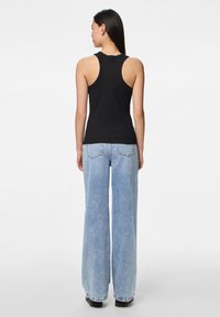 Černý bavlněný top bez rukávů s designem na závodní záda, spárovaný se světle modrými širokými džíny, které mají vybledlou texturu a zadní kapsy.