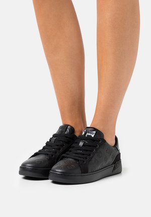 Baskets noires en matériau texturé avec logos en relief. Elles comportent des lacets plats noirs et des semelles en caoutchouc, avec un design à profil bas.