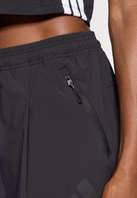 Svarte treningshorts med elastisk liv, med en glidelås-lomme på siden og glatt tekstur. Diskret logo på leggen.