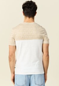 Lyhythihainen t-paita, jossa on vaaleanbeige ja valkoinen kuviollinen yläosa, joka siirtyy yksinkertaiseen valkoiseen alaosaan. Pehmeää puuvillakangasta.