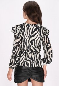 Bluse mit schwarz-weißem Zebra-Muster und Rüschensleeves; durchsichtiges Gewebe mit leichtem Glanz; geraffte Taille; kombiniert mit einem schwarzen, gerafften Rock.